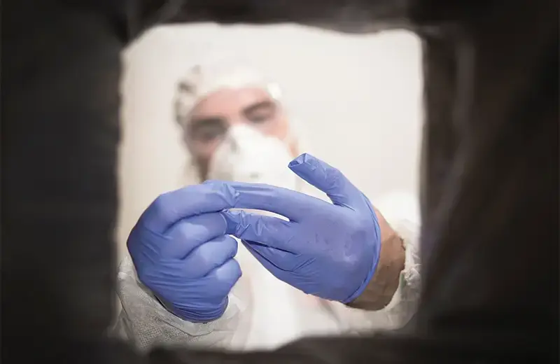 A person in protective gear removing a latex glove
